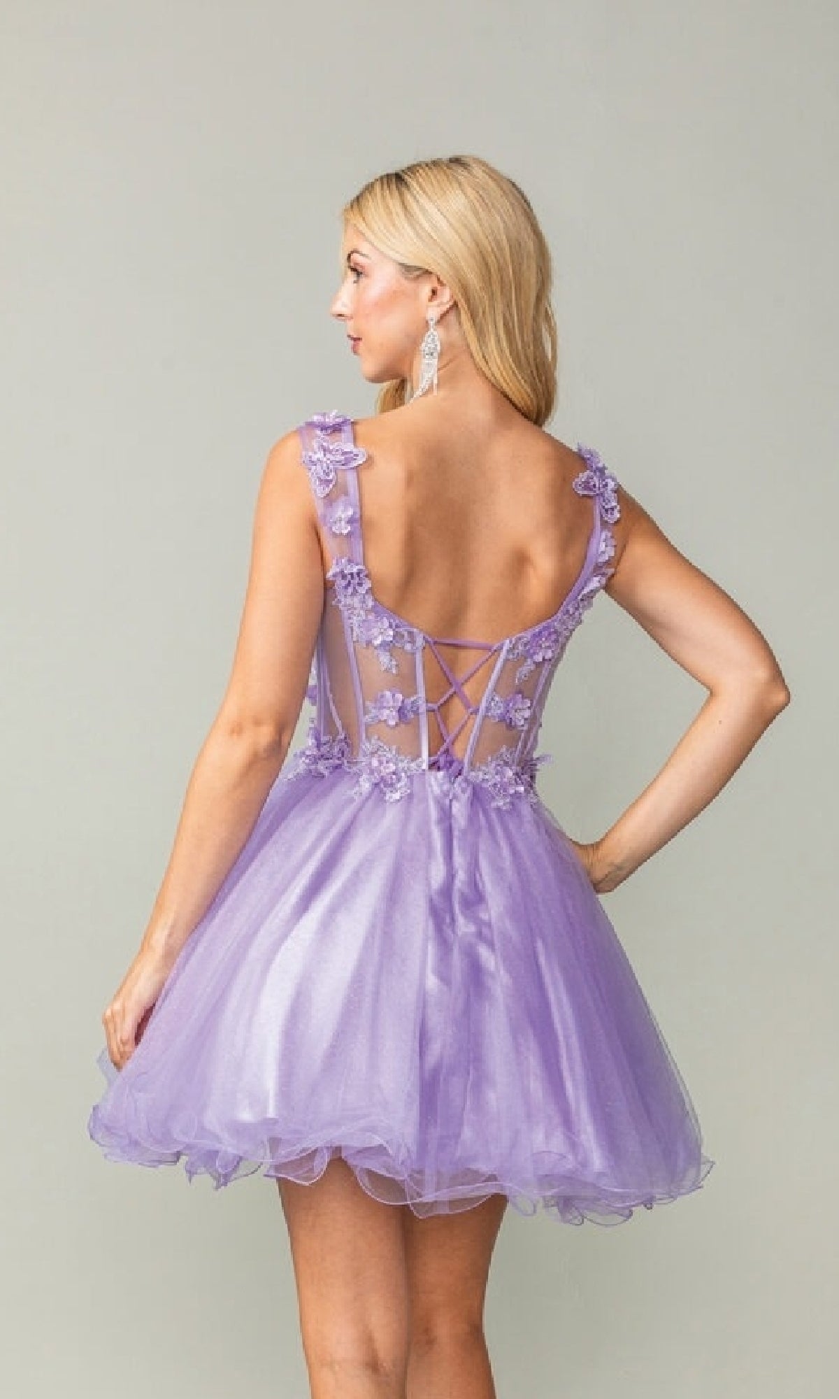 Woman showing the back of a short lilac dress with intricate back design that she's wearing, on a plain background
